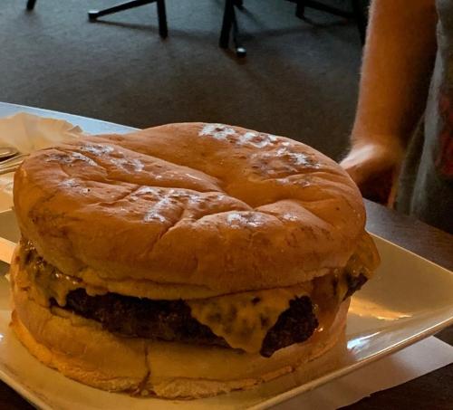 A large cheeseburger with a thick patty and melted cheese, served on a plate in a casual dining setting.