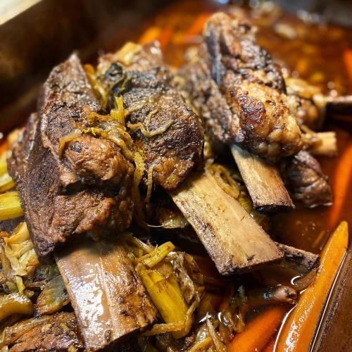 Close-up of tender, braised beef short ribs served over a bed of sautéed greens and carrots in a rich sauce.