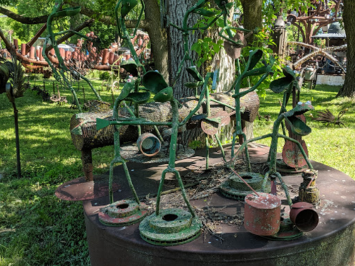 A whimsical outdoor sculpture garden featuring metal figures resembling plants and musicians among greenery.