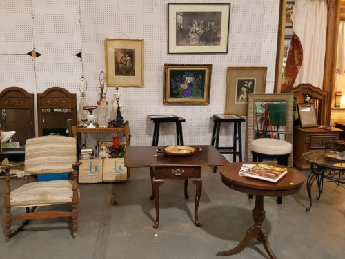 A vintage shop display featuring various furniture pieces, framed art, and decorative items on a pegboard wall.