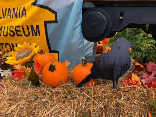 A display featuring pumpkins, sunflowers, and a black crow silhouette on a hay bale, with a yellow banner in the background.