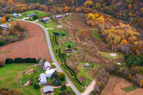 Aerial view of a rural landscape with farms, fields, and autumn-colored trees along a winding road.