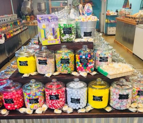 A colorful display of various candies in glass jars, arranged on a wooden stand with a festive atmosphere.