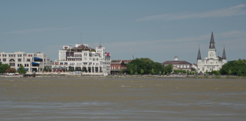 View of a riverside cityscape featuring historic buildings and churches under a clear blue sky.