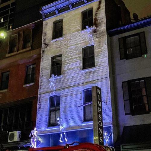 A building with skeleton decorations climbing its exterior, illuminated by blue lights at night.