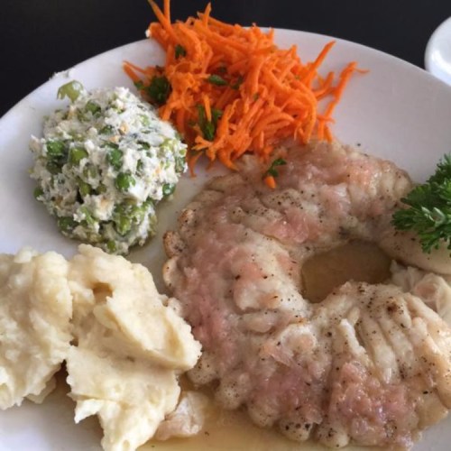 A plate featuring fish fillet, mashed potatoes, carrot salad, and a green pea salad with herbs.