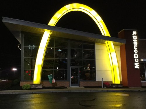 A brightly lit McDonald's restaurant at night, featuring the iconic golden arches and a modern glass facade.