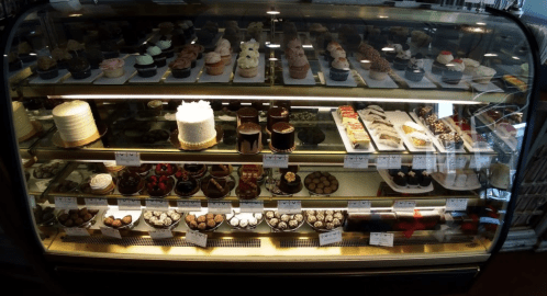 A display case filled with various desserts, including cupcakes, cakes, chocolates, and pastries.