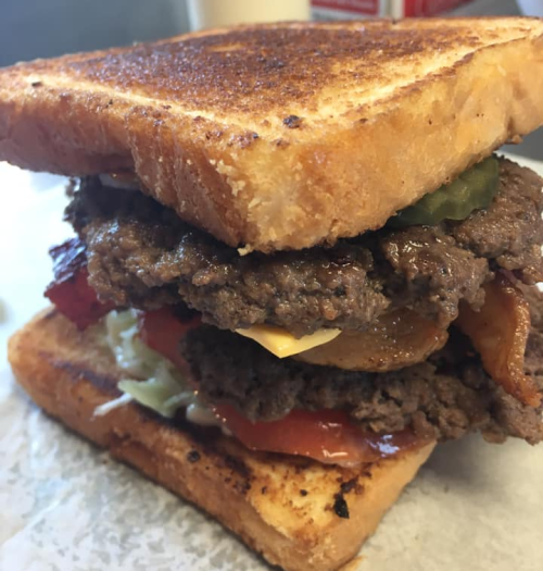 A stacked burger with two beef patties, cheese, lettuce, tomato, pickles, and toasted bread.