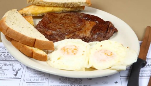 A plate with a steak, two fried eggs, and slices of bread, served on a table with a menu underneath.