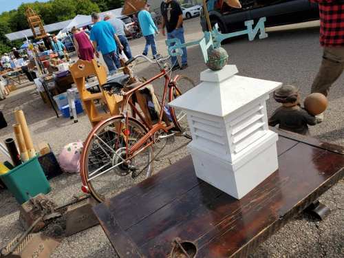 A vintage market scene featuring a white lantern, a bicycle, and various items for sale on a wooden table.