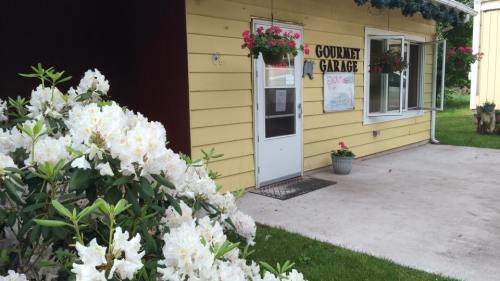 A yellow building with a sign reading "Gourmet Garage," surrounded by flowers and greenery.