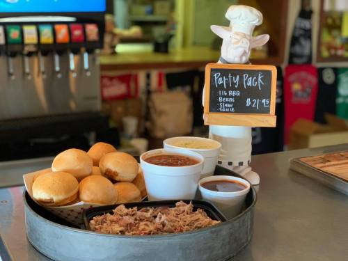 A tray with pulled pork, beans, coleslaw, and rolls, next to a sign for a BBQ party pack priced at $21.95.