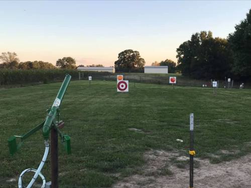 A grassy field with multiple targets set up for shooting practice, surrounded by trees and a clear sky.