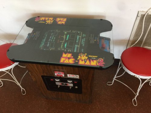 A Ms. Pac-Man arcade table with a glass top, surrounded by two red chairs in a retro setting.