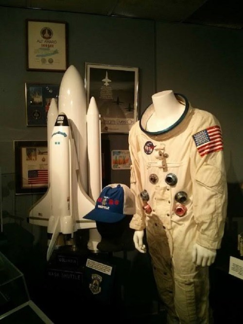 A display featuring a NASA astronaut suit, a shuttle model, and a cap, showcasing space exploration memorabilia.