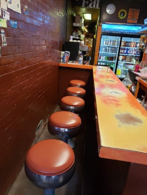 A cozy diner interior featuring a counter with orange stools and a colorful, worn countertop.