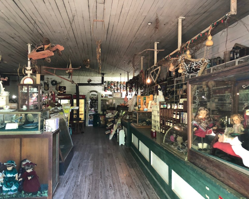 Interior of a vintage shop filled with antiques, dolls, and various collectibles, featuring wooden floors and rustic decor.