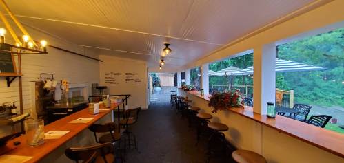 A cozy café interior with wooden stools, a long counter, and large windows overlooking a rainy outdoor area.