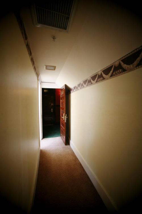 A dimly lit hotel hallway with a partially open door at the end, revealing a glimpse of a room.