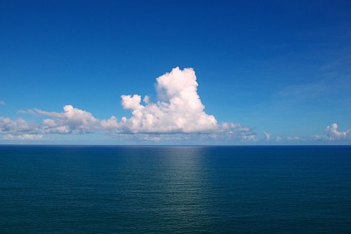 A serene ocean view with calm blue waters and fluffy white clouds against a bright blue sky.
