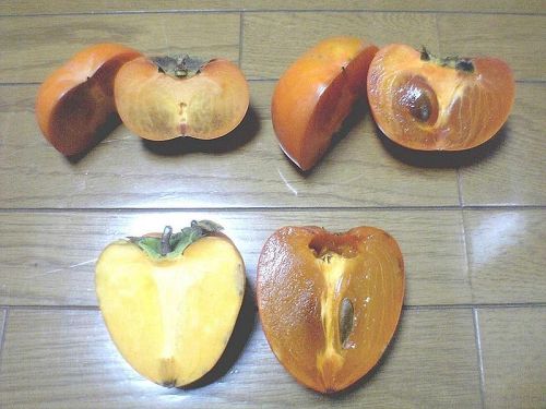 Two whole persimmons and two halved persimmons, showcasing their vibrant orange color and seeds, on a wooden surface.