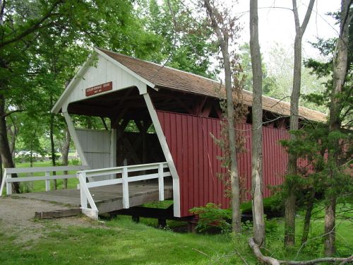 A red and white covered bridge surrounded by trees, with a wooden walkway leading through it.