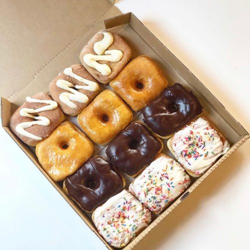 A box of assorted donuts, featuring glazed, chocolate, and frosted varieties with sprinkles.