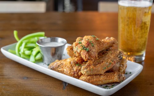 A plate of crispy fried chicken wings with celery sticks and ranch dressing, alongside a glass of beer.