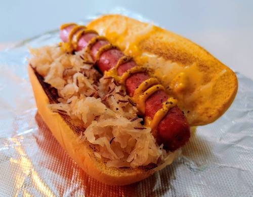 A hot dog in a toasted bun topped with mustard and sauerkraut, served on aluminum foil.