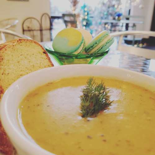A bowl of creamy soup garnished with dill, accompanied by a slice of bread and colorful macarons in a green dish.