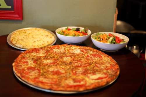 A large pepperoni pizza on a table, accompanied by two bowls of colorful salads.