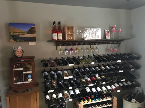 A wine rack filled with various bottles, glasses hanging above, and a decorative shelf with a scenic photo and a figurine.