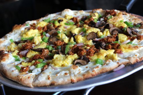 A pizza topped with scrambled eggs, sausage, mushrooms, green peppers, and onions on a golden crust.