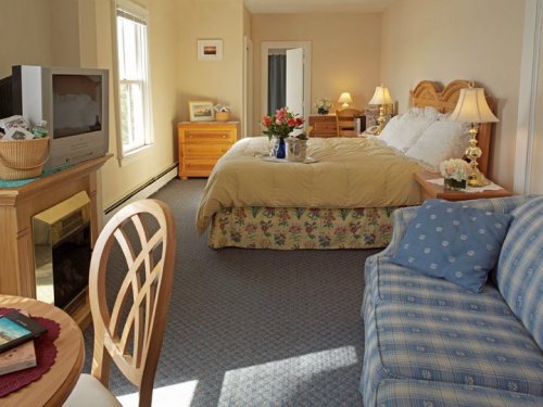Cozy bedroom with a queen bed, floral decor, a TV, and a seating area with a blue couch and dining table.