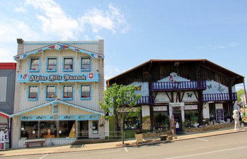 Two distinct buildings side by side: the Alpine Hills Museum with blue accents and a rustic shop with a wooden facade.
