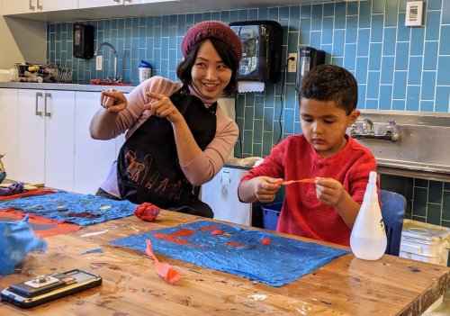 A woman and a boy are crafting at a table, smiling and engaging with colorful materials in a creative space.