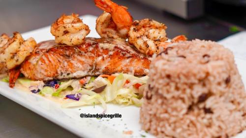 Grilled salmon topped with shrimp, served on a bed of cabbage with a side of rice and beans.
