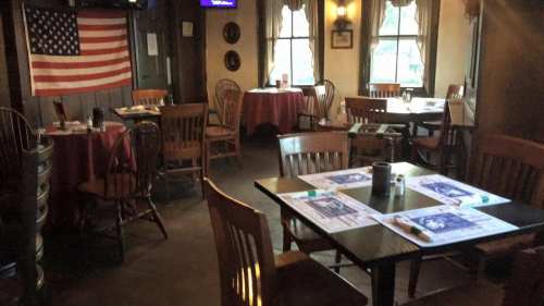 Cozy restaurant interior with wooden tables, chairs, and an American flag on the wall.