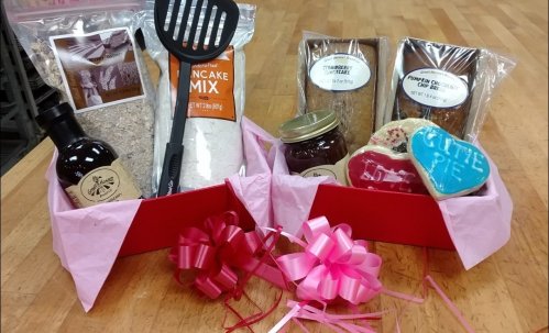 Gift boxes filled with pancake mix, jam, baked goods, and decorated cookies, arranged with pink ribbons.