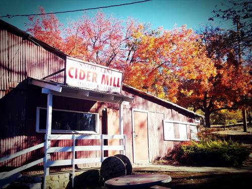 A rustic cider mill with a sign, surrounded by vibrant autumn foliage in shades of red and orange.