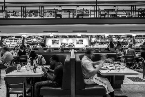 A bustling restaurant scene in black and white, featuring diners at booths and a bar in the background.