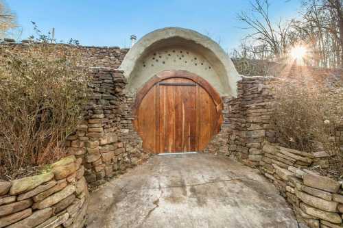 A round wooden door set in a stone wall, resembling a hobbit hole, surrounded by trees and sunlight.