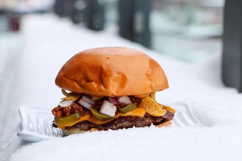 A delicious burger with cheese, toppings, and crunchy chips, resting on a snowy surface.