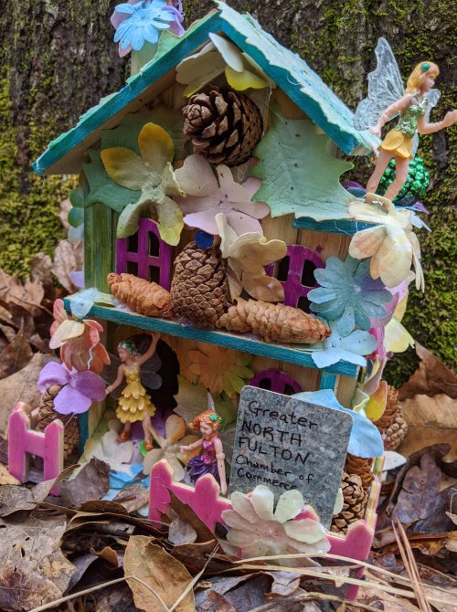 A whimsical fairy house made of natural materials, adorned with flowers and tiny fairy figurines, nestled among leaves.