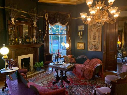A cozy, vintage living room with ornate furniture, a chandelier, and a fireplace, adorned with rich colors and decor.