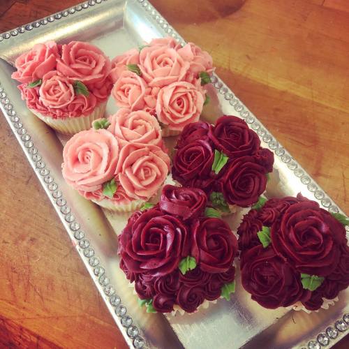 A silver tray holds six beautifully decorated cupcakes shaped like pink and red roses.