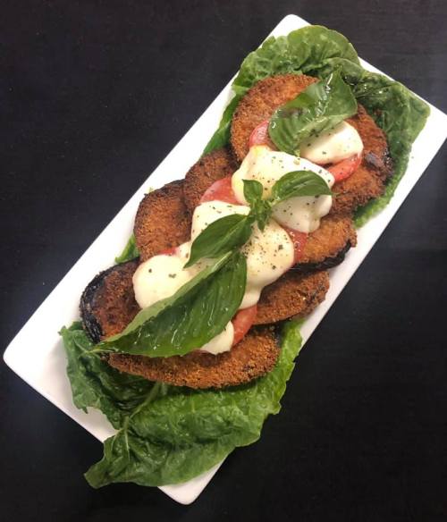 A platter of crispy fried eggplant slices topped with tomato, mozzarella, and fresh basil on a bed of lettuce.