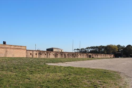 Historic brick fort with arched openings, set against a clear blue sky and grassy foreground.