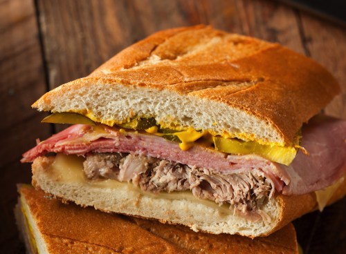 A close-up of a sandwich with layers of meats, cheese, pickles, and mustard on toasted bread.
